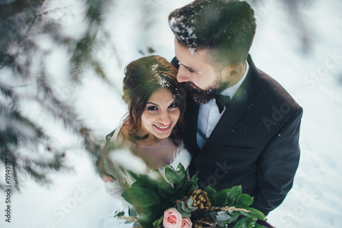 Bearded man and his lovely bride pose on the snow in a magic winter forest