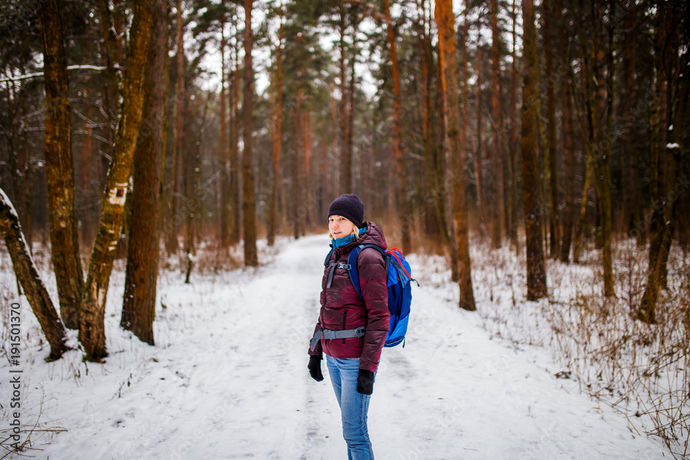 Photo of side view of smiling girl in hat with backpack over winter forest