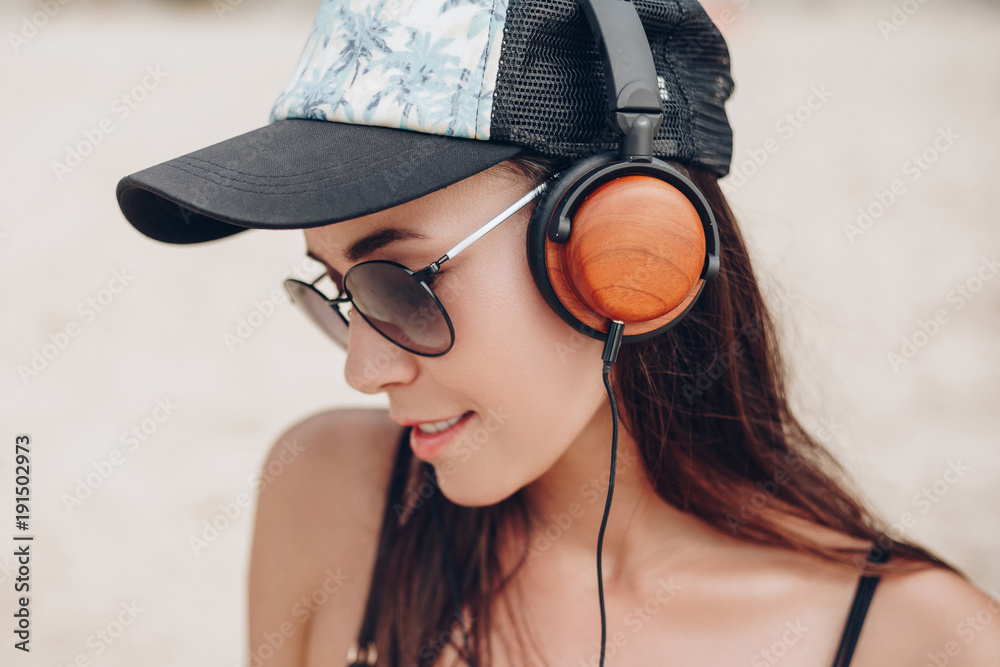 Naklejka premium beautiful young woman in cap and sunglasses listening music with headphones