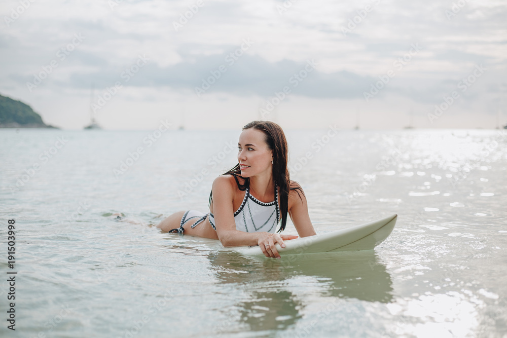 beautiful young woman in swimsuit lying on surfboard in water