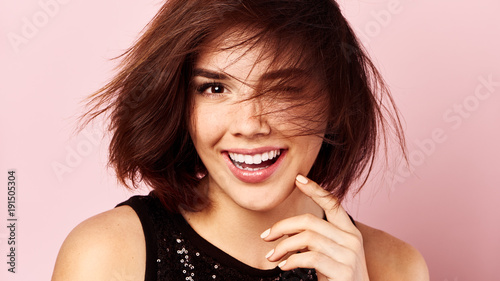 Beauty portrait of happy smiling female model with disheveled hair over pink background.  photo