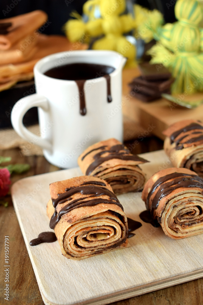 Crepes rolls with chocolate sauce on a wooden board Crepes rolls with chocolate sauce on a wooden board