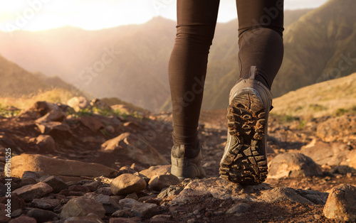 Close up of hiker boots trekking in the mountains at the sunrise with copy space