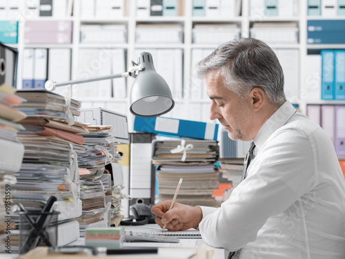 Businessman working in the office and piles of paperwork photo