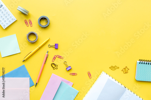 Scattered stationery on student's desk. Yellow background top view copy space