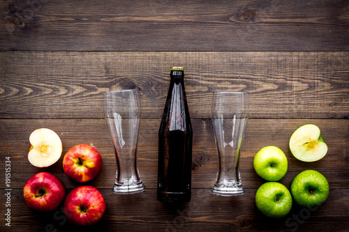 Apple cider. Low-alcoholic beveradge in dark bottle near beer glasses and fresh apples on dark wooden background top view copy space