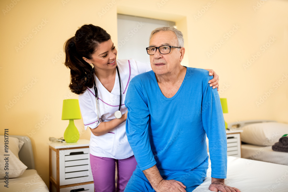 Obraz premium Very patient nurse helps old senior man to stand up from bed