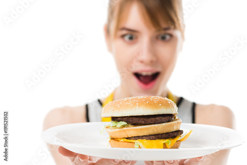 excited young woman looking at burger on plate isolated on white