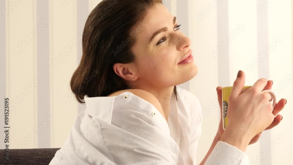 woman holding a mug of hot tea sitting on a sofa woman holding a mug of hot tea sitting on a sofa