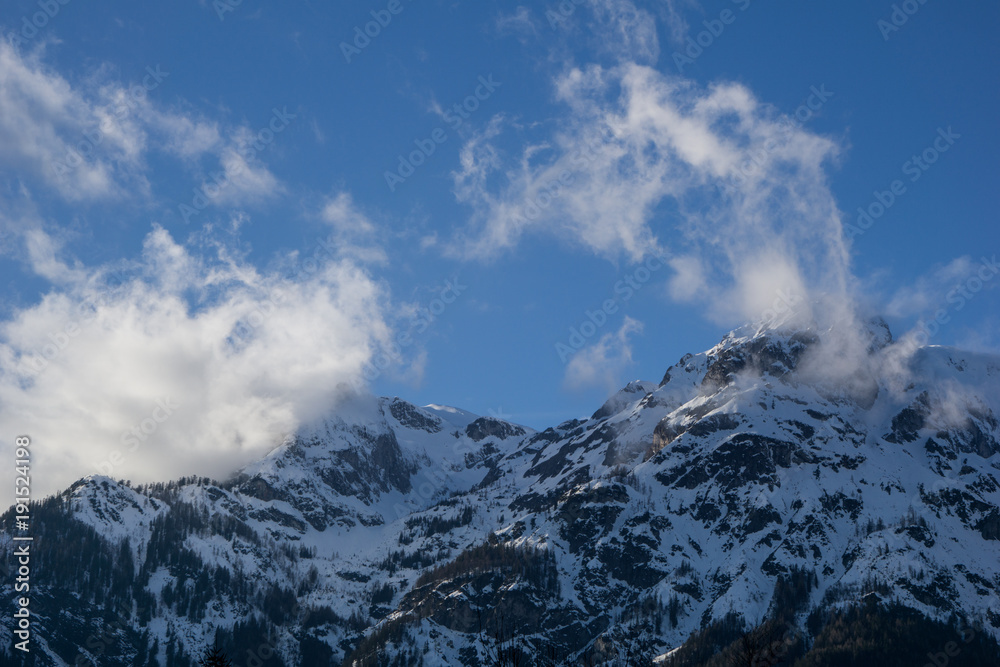 Tall, snow covered alpine peaks meeting the clouds on a clear day with blue skies