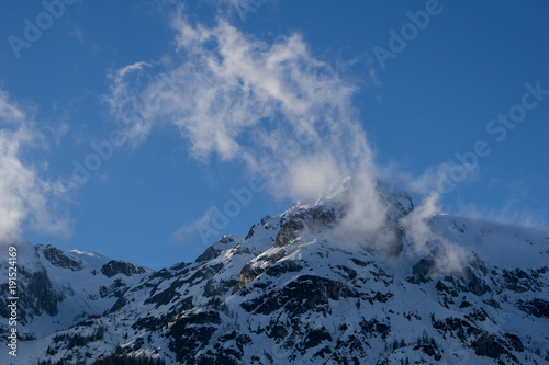 Wind swept, snowy mountain peak on a clear blue sky background