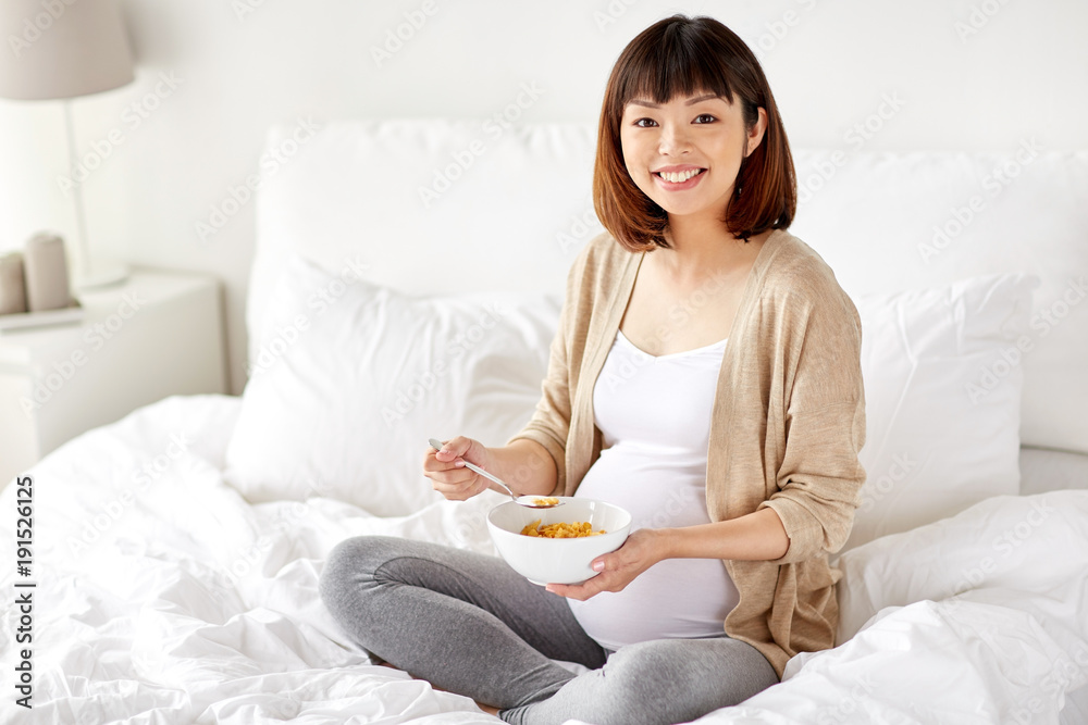 happy pregnant woman eating cereal flakes at home