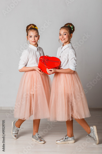 Cute curious twins sisters unpacking red heart shaped gift. Celebrating saint valintine's day.