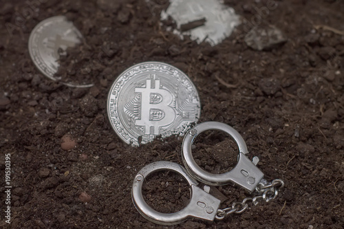 The concept of illegal bitcoin mining. Crypto currency is illegal. Coin and handcuffs on the ground
