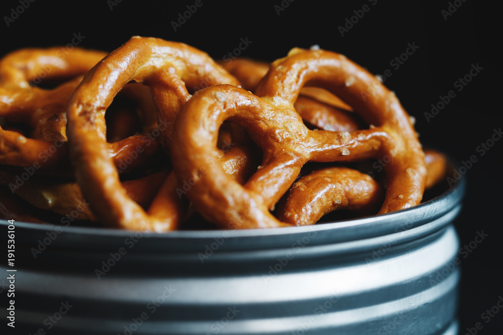 Crunchy pretzels appetizer in a metal jar against black background. Macro shot. Crunchy pretzels appetizer in a metal jar against black background. Macro shot.