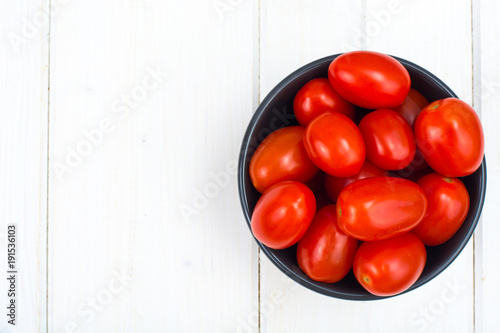 Small red ripe tomatoes in bowl on wooden table, top view