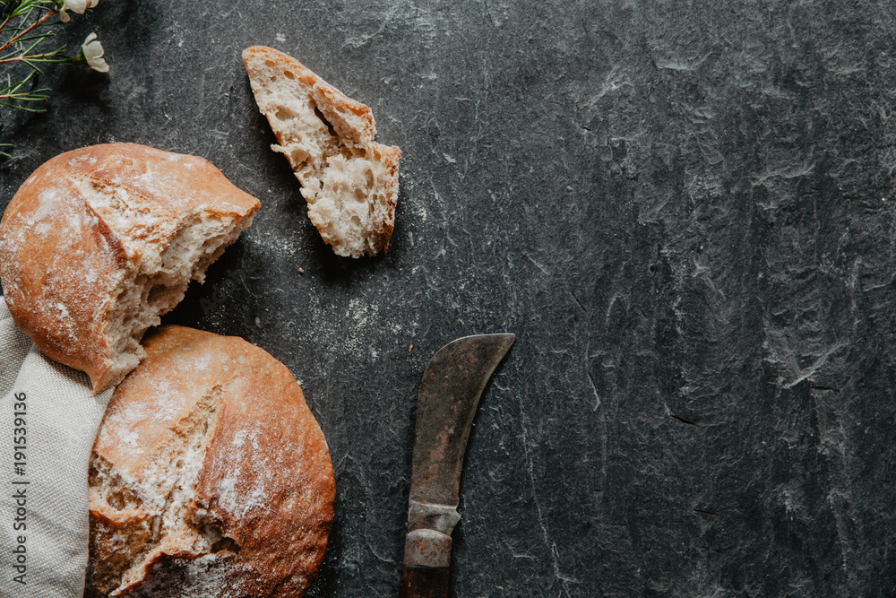 Slices of homemade bread with knife and little white flowers on black stone Slices of homemade bread with knife and little white flowers on black stone
