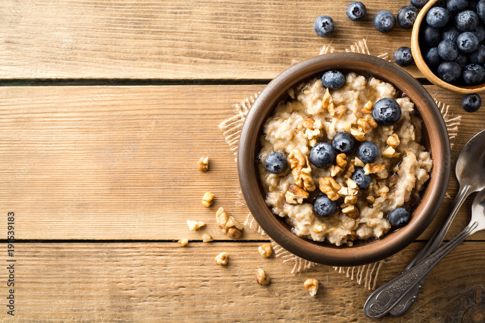 Oatmeal porridge with blueberries, walnuts and honey in ceramic bowl on wooden background. Oatmeal porridge with blueberries, walnuts and honey in ceramic bowl on wooden background.
