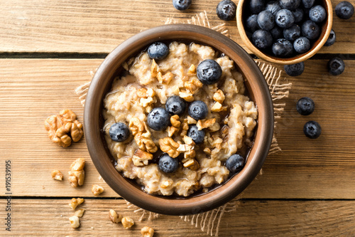 Oatmeal porridge with blueberries, walnuts and honey in ceramic bowl on wooden background. photo
