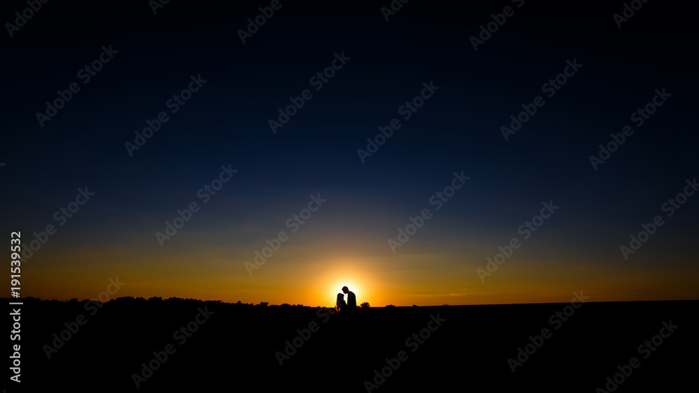 Silhouette of a loving couple over sunset background. a guy and a girl hug and kiss on the horizon in front of the sun