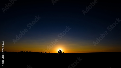 Silhouette of a loving couple over sunset background. a guy and a girl hug and kiss on the horizon in front of the sun