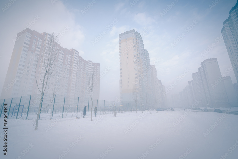 Foggy winter cityscape. Foggy city street with silhouettes of high residential buildings.