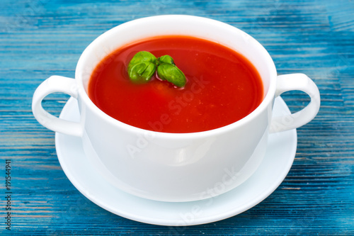 Cream soup of fresh red tomatoes on blue wooden background