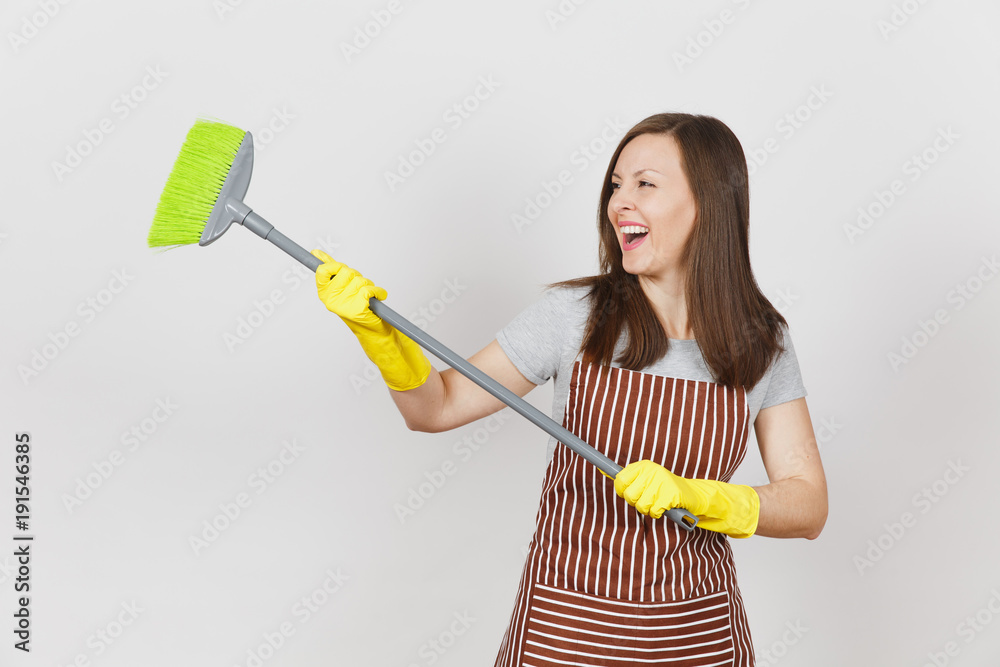Young smiling housewife in striped apron, yellow gloves isolated on white background. Fun housekeeper woman cleaning maid holding and sweeping with broom. Copy space for advertisement Advertising area Young smiling housewife in striped apron, yellow gloves isolated on white background. Fun housekeeper woman cleaning maid holding and sweeping with broom. Copy space for advertisement Advertising area