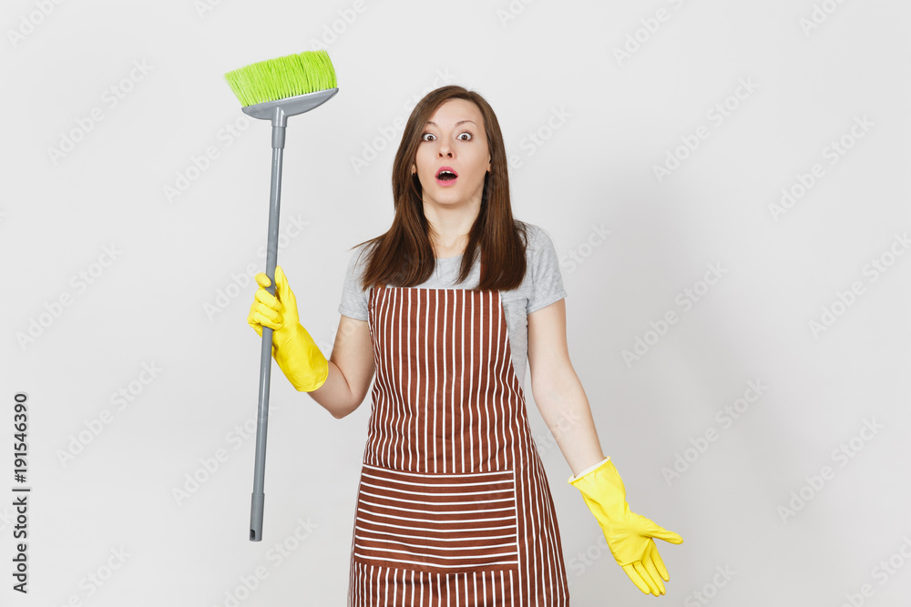 Young shocked housewife in striped apron, yellow gloves isolated on white background. Housekeeper woman cleaning maid holding and sweeping with broom. Copy space for advertisement. Advertising area. Young shocked housewife in striped apron, yellow gloves isolated on white background. Housekeeper woman cleaning maid holding and sweeping with broom. Copy space for advertisement. Advertising area.
