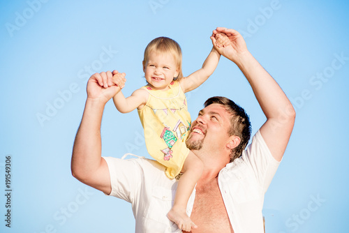 Portrait of happy man holding his little daughter on neck on the background of sky