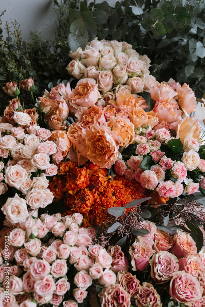 Fototapeta premium Fresh flower delivery at the florist shop: different flowers stocked up together, orange red and paster colours; different types of roses and ranunculus with eucalyptus on the background