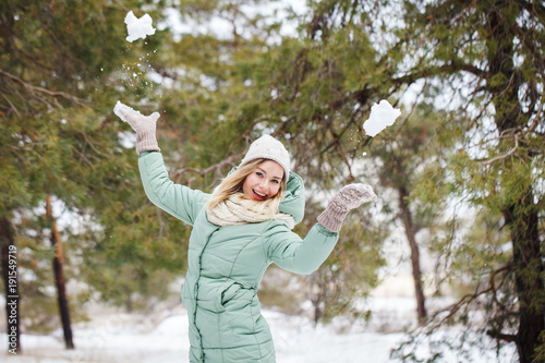 Attractive beautiful girl throws snow up her hands and laughs. Portrait of a slender cute girl on a winter background, looking at the camera and smiling. Space for text