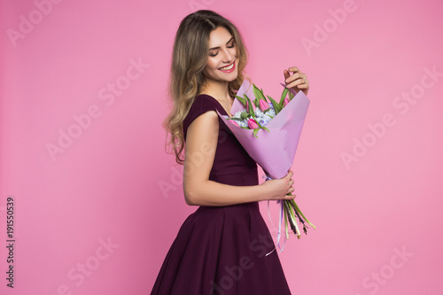 Charming, pretty girl is holding a big tulip bouquet in hands. Pink background. Happy woman's day