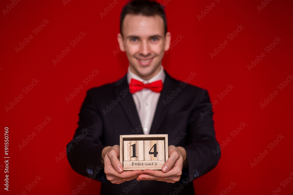 Stylish man in suit hold wooden calendar, set on 14 February with red background, focus on calendar. Valentines day composition Stylish man in suit hold wooden calendar, set on 14 February with red background, focus on calendar. Valentines day composition