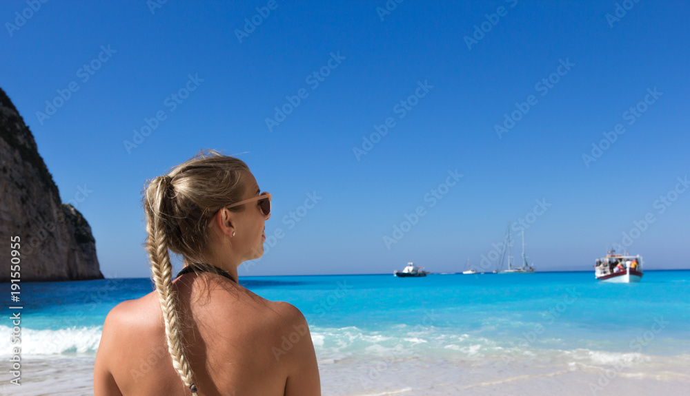 Junge blonde Frau an einem Strand mit türkisblauem Wasser