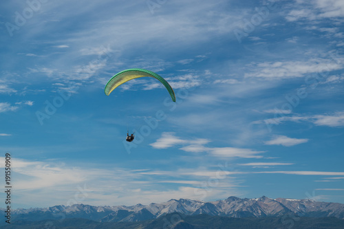 Paraglider green color flying high with snowy mountains background
