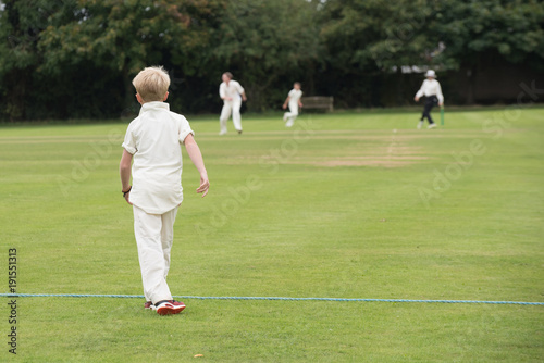 young English school cricket player waits on the boundary with umpire in the background