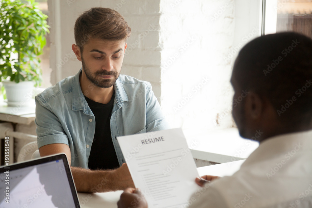 Stressed caucasian applicant feels worried while african hr employer reading resume, stress at job interview concept, nervous anxious man candidate waiting for result at hiring employment negotiation Stressed caucasian applicant feels worried while african hr employer reading resume, stress at job interview concept, nervous anxious man candidate waiting for result at hiring employment negotiation
