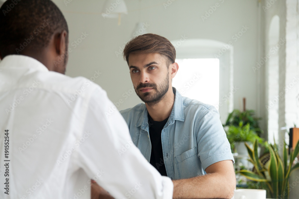 Serious attentive businessman listening to african partner at negotiations, focused caucasian entrepreneur thinking considering decision at business discussion with black colleague in office teamwork