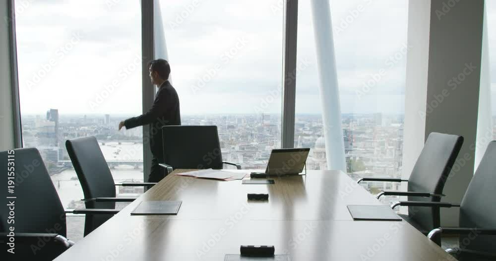 4K Worried businessman working alone in office boardroom, pacing in front of the window with city view in background