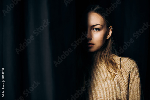 Portrait near a black curtain of an attractive blue-eyed woman that only shows half of her face