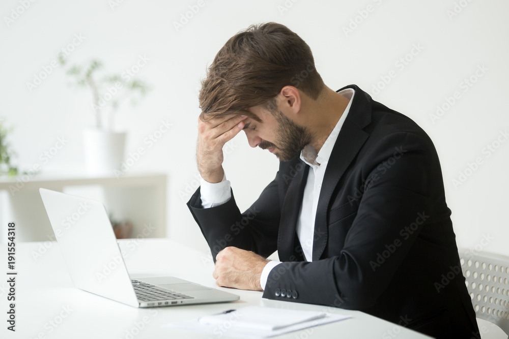 Depressed unsuccessful businessman feels terrible headache, distraught stressed entrepreneur regrets of business mistake shocked by bankruptcy desperate after failure sitting at work desk with laptop Depressed unsuccessful businessman feels terrible headache, distraught stressed entrepreneur regrets of business mistake shocked by bankruptcy desperate after failure sitting at work desk with laptop