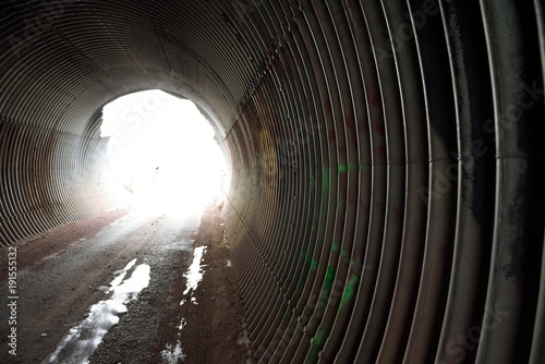 Path into bright light at the end of a round metal pipe tunnel.