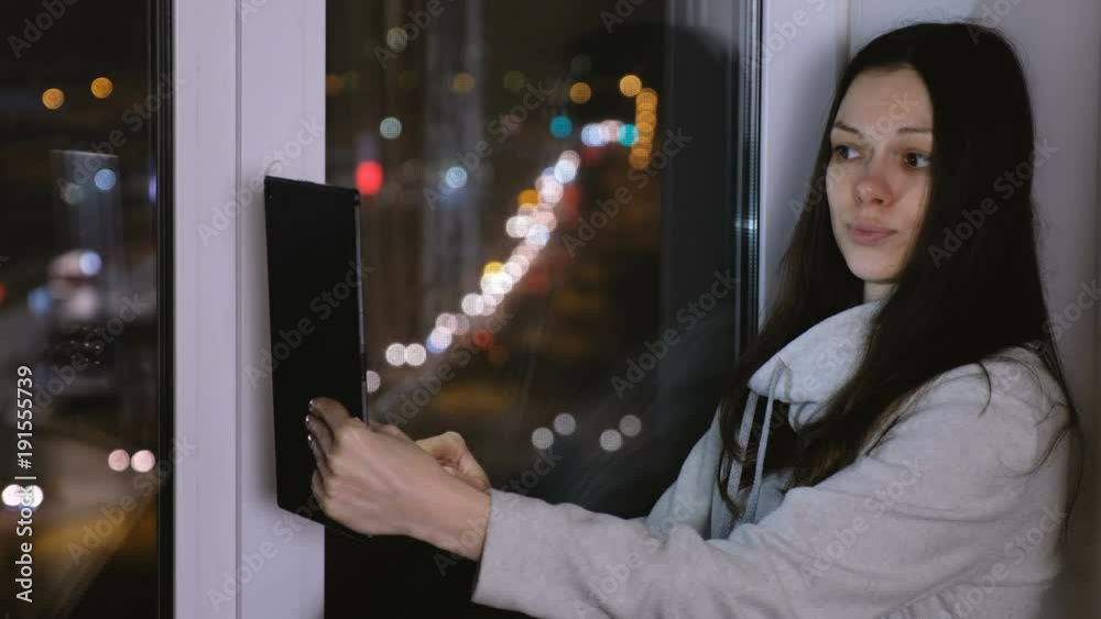 Woman is sitting on the windowsill in the dark night and doing selfies on tablet. Woman is sitting on the windowsill in the dark night and doing selfies on tablet.