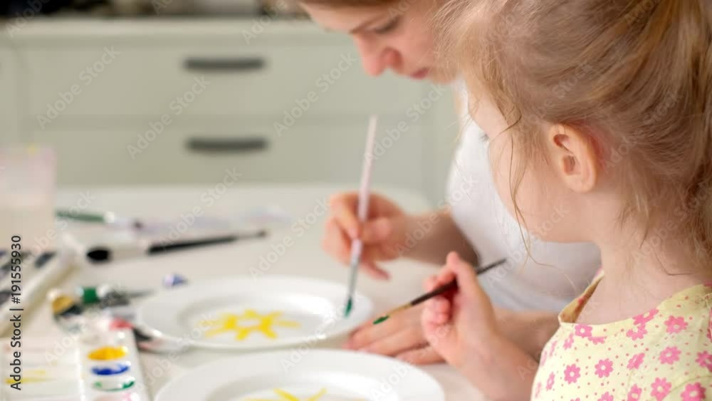 Happy family, mother and little daughter paint with paint on white plates Happy family, mother and little daughter paint with paint on white plates