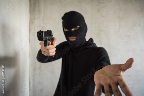 Masked robber with gun aiming into people