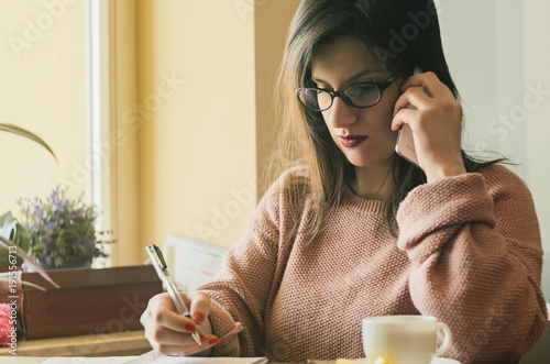 A young beautiful serious women making a phone call and taking notices as a business woman