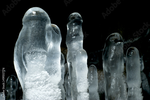 group of transparent ice stalagmites in a cave closeup on a dark background photo