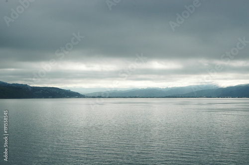 A stormy sky over a lake. The sun is breaking through the clouds, turning the water silver. The scene is deserted.