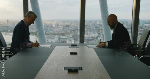4K Mature business managers exchanging contracts & shaking hands on a deal. City office boardroom with panoramic view of London.